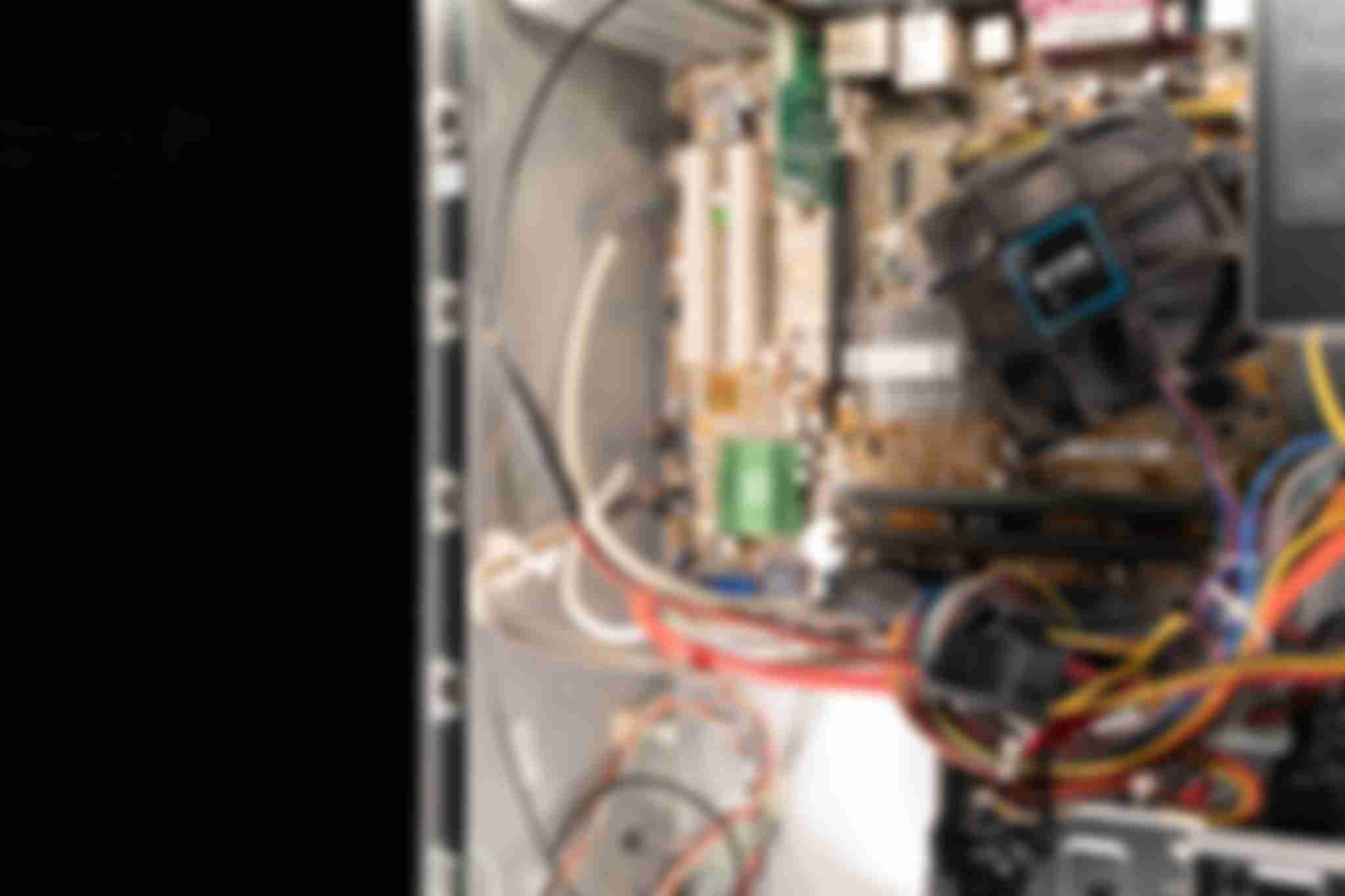 A close-up of well lit internal computer parts of a desktop computer. It shows a fan, part of the motherboard, RAM sticks and other electrical components.