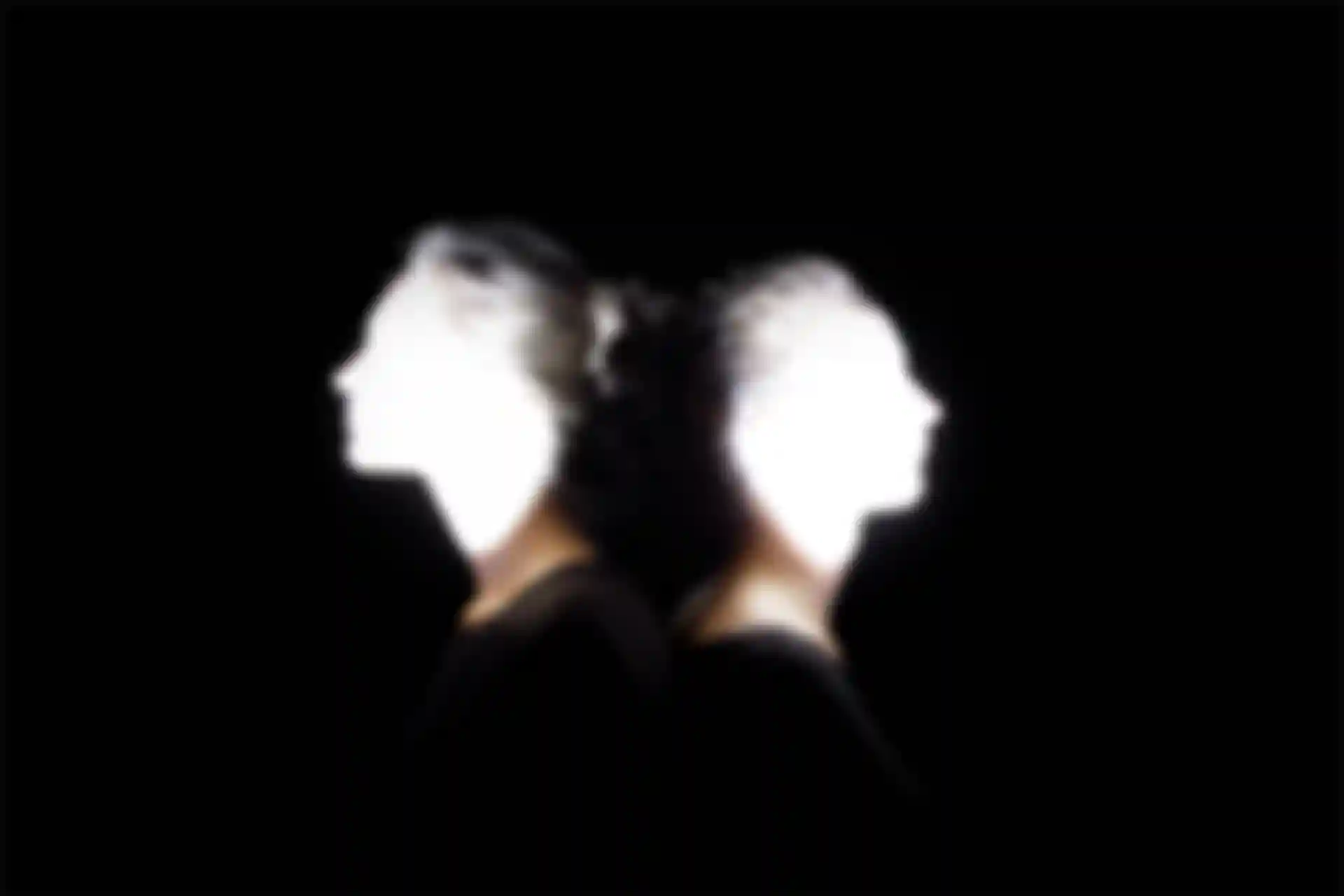 Zwei Frauen stehen Rücken an Rücken mit überbelichteten Gesichtern.