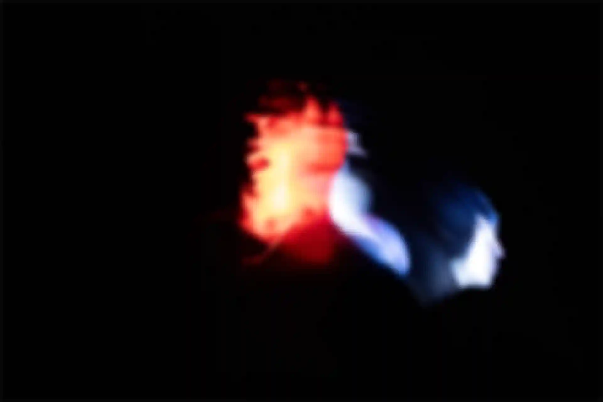 Ein Mann hat ein überbelichtetes Gesicht von zwei Lichtquellen. Eine blaue und eine rote Lichtquelle.